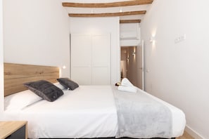 A bedroom with a wooden headboard, white bedding, a grey blanket, and a white towel on the bed.