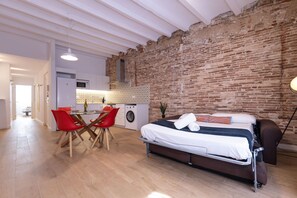 A modern room with a bed, a dining table with chairs, a washing machine, and a brick wall. - Merceria 3 by Unik Tarragona (Tarragona)