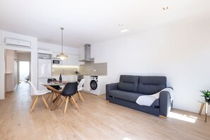 A modern kitchen with a dining area, a gray sofa, and a small side table with a plant. - Merceria 3 by Unik Tarragona (Tarragona)