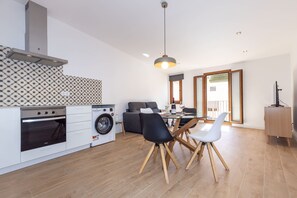 A modern kitchen with a built-in oven, a washing machine, and a dining area with a table and chairs.