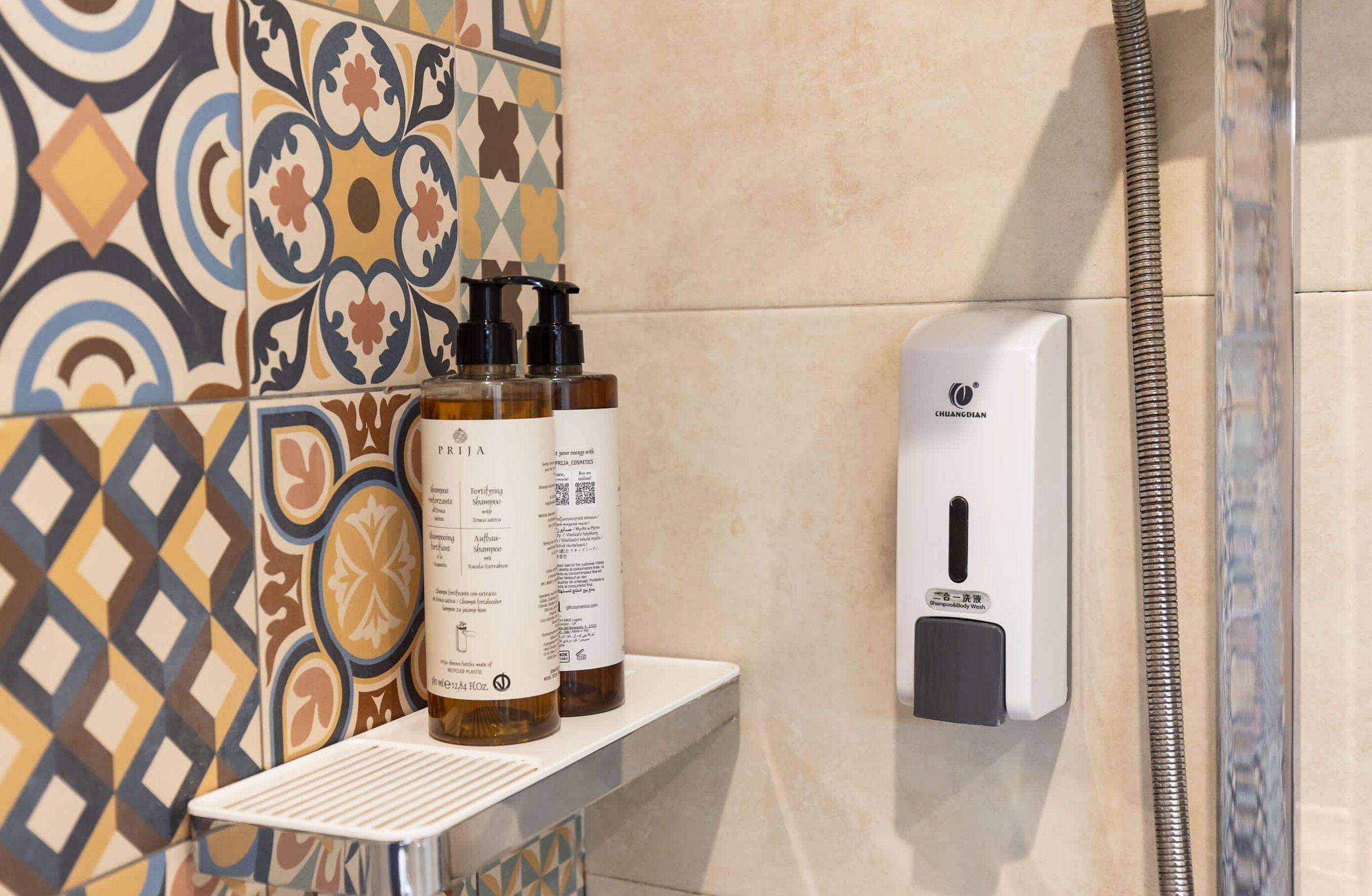 Un baño con azulejos estampados, un dispensador de jabón y dos botellas de champú.