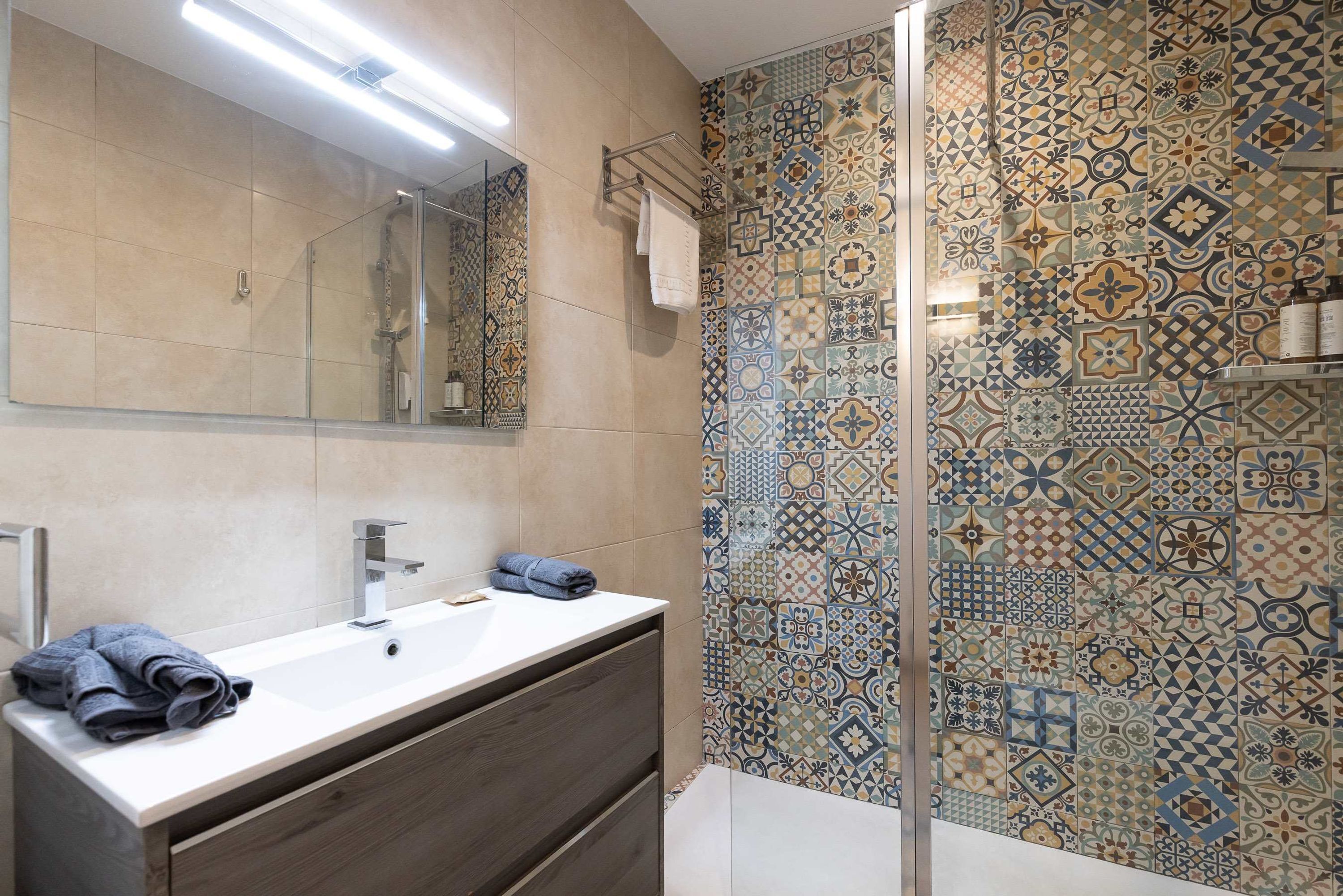 A bathroom with a large mirror, a white sink, and a shower area.