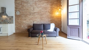 A living room with a brick wall, a sofa, a glass coffee table, and a wooden floor. - Merceria 1 by Unik Tarragona (Tarragona)