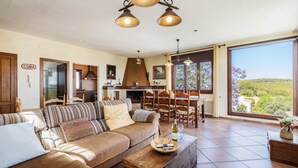 Amplia sala de estar con sofá, mesa de comedor y ventanas grandes que ofrecen vistas al campo.