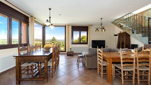 Un salón amplio con una mesa de comedor, sillas de madera, un sofá, un televisor y una escalera.