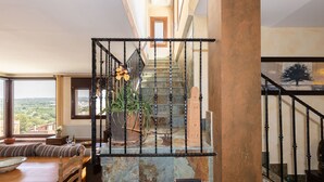 Una escalera con barandilla de metal, vistas al exterior, un comedor con mesa y sillas, y una planta en maceta.