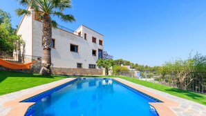 Una piscina con borde de azulejos, un edificio blanco con múltiples ventanas y una palmera.