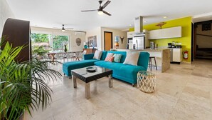 A spacious living area with a teal sofa, a glass coffee table, and a dining area with chairs and a table. - 3BR Family Condo, Pool, Walk to Beach – Sayulita | Casa de Paz (Sayulita)