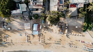 An aerial view of a beach with rows of sun loungers and umbrellas, a small building, and palm trees. - 3BR Family Condo, Pool, Walk to Beach – Sayulita | Casa de Paz (Sayulita)