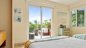 A bedroom with a large bed, a sliding glass door leading to a balcony with outdoor furniture and plants. - 3BR Family Condo, Pool, Walk to Beach – Sayulita | Casa de Paz (Sayulita)