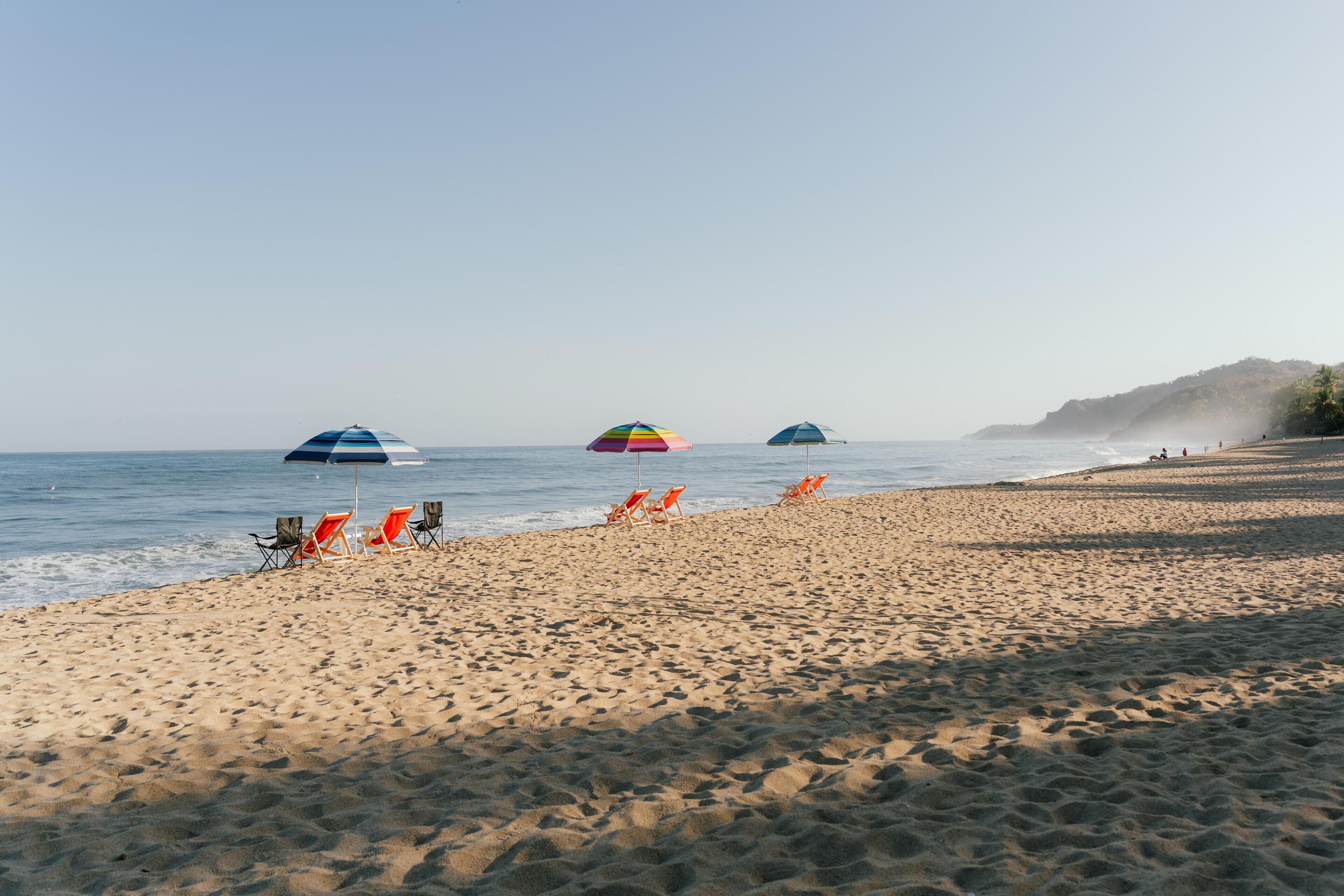 A beach with rows of orange lounge chairs and umbrellas, a calm sea, and a clear sky.