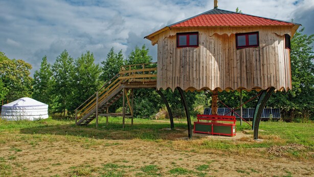 Een houten boomhut met een rood dak, een houten trap en een zonnepaneel.