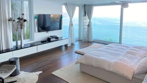 A modern bedroom with a large bed, a TV, and a view of the sea. -  Luxury Ocean Front Loft in Rio De Janeiro Joa (Joá Rio de Janeiro)