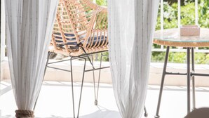 A balcony with a wicker chair and a small table, draped with sheer white curtains.