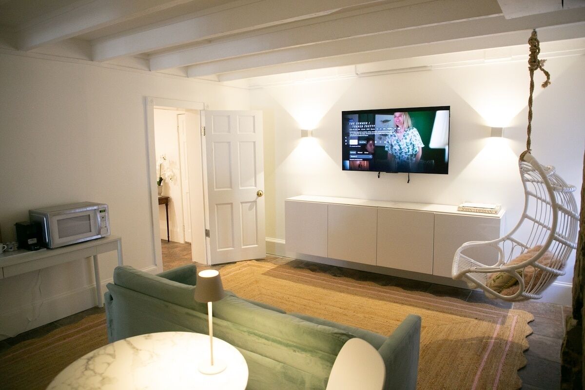 Un salon comprenant un téléviseur, un canapé, un fauteuil suspendu, une petite table et un four à micro-ondes posé sur un meuble.