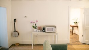 Een kamer met een witte muur, een witte tafel met een magnetron, een banjo en een potorkidee.