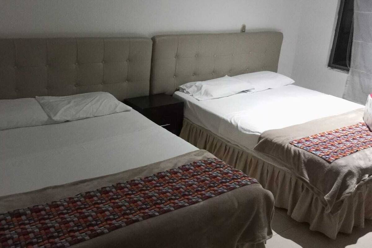 A room with two beds, each with a headboard and a white bedspread. There is a small table between the beds.