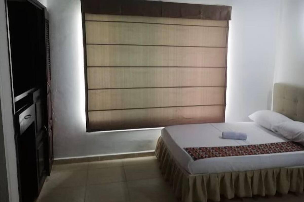 A bedroom with a bed, a window with blinds, a bedside table, and a nightstand.