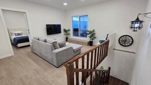 Una sala de estar moderna con un sofá gris, un televisor de pantalla plana y una escalera con barandillas de madera.