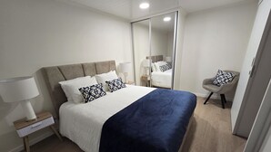 Un dormitorio ordenado con cama, lámparas de noche, una silla y un espejo.