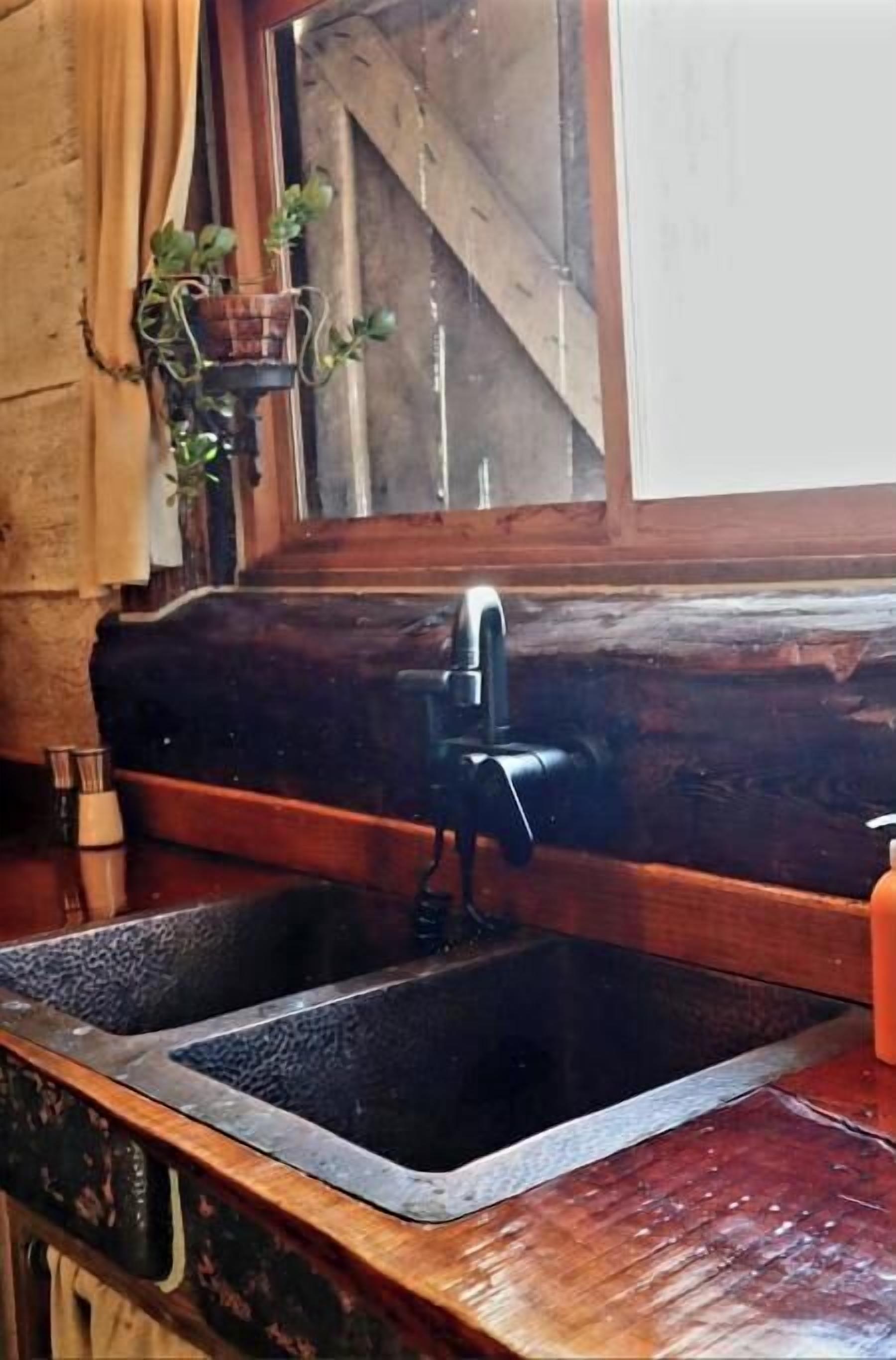 A kitchen with a wooden countertop, a black sink, and a window with a view of a wooden structure outside.