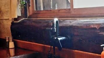A kitchen with a wooden countertop, a black sink, and a window with a view of a wooden structure outside.