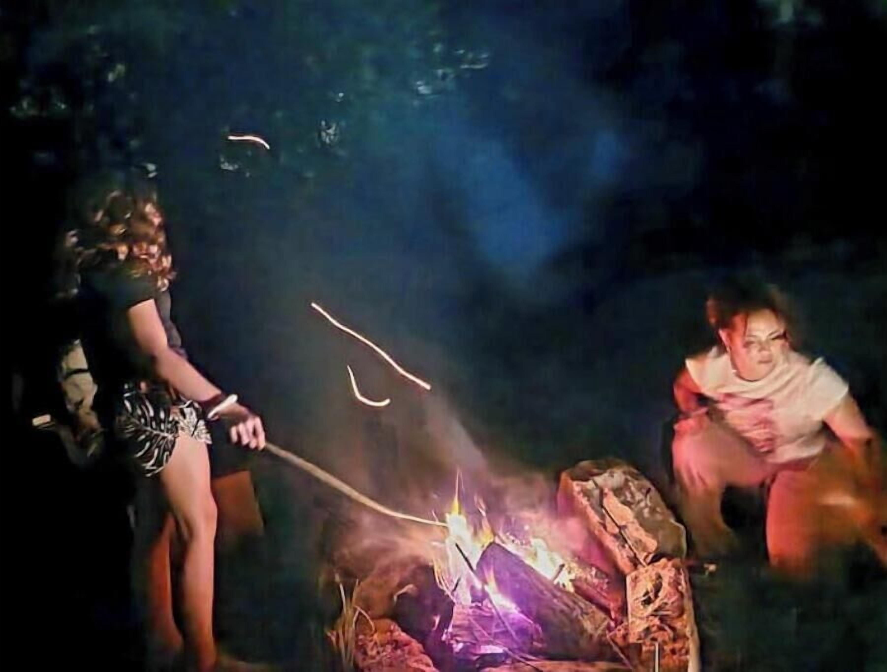 Two people around a campfire at night.