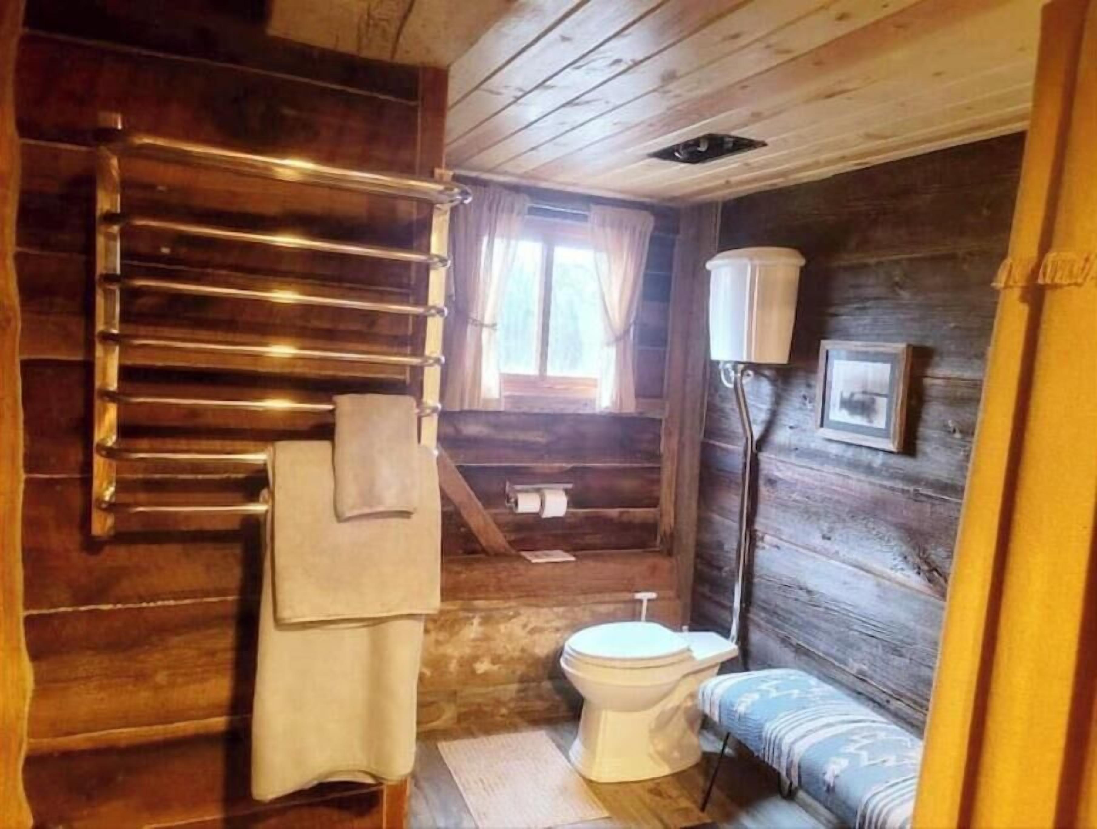 Puisesta hirrestä rakennettu kylpyhuone, jossa on puinen kylpyamme, wc ja penkki.