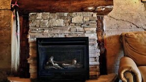 A stone fireplace with a metal grate, wooden beams, and a brown leather couch. - Rustic Luxury w/Horses-Historic Whiskey Distillery (Watsontown)