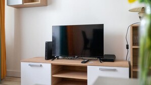 Una sala moderna con un televisor de pantalla plana sobre un mueble de madera, un armario blanco y una mesita con un control remoto.