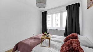 Un dormitorio moderno con una cama, una mesita de noche con una bandeja y un objeto rojo y esponjoso sobre la cama.