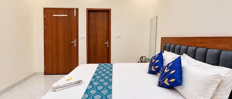 A hotel room with a bed, a wooden wardrobe, a mirror, and a bedside table with a kettle and a bottle.