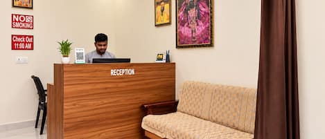 Un área de recepción con un mostrador de madera identificado con 'RECEPTION', un sofá, una alfombra estampada y dos cuadros en la pared.