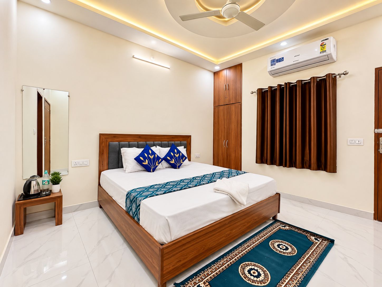 Habitación de hotel con cama, mesita de noche, aire acondicionado, espejo, armario y alfombra estampada.