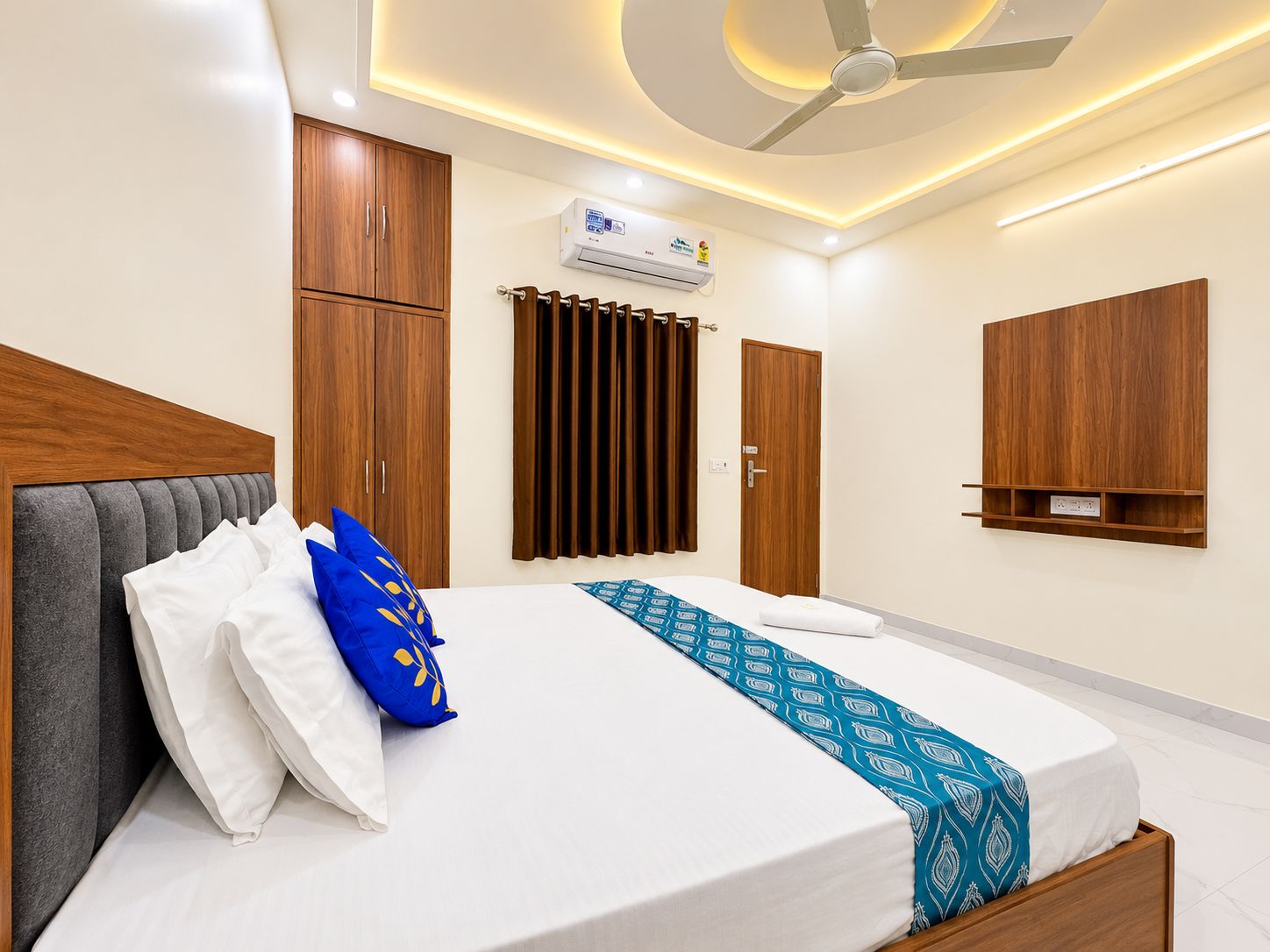 A hotel room with a bed, wardrobe, air conditioning unit, and a ceiling fan.