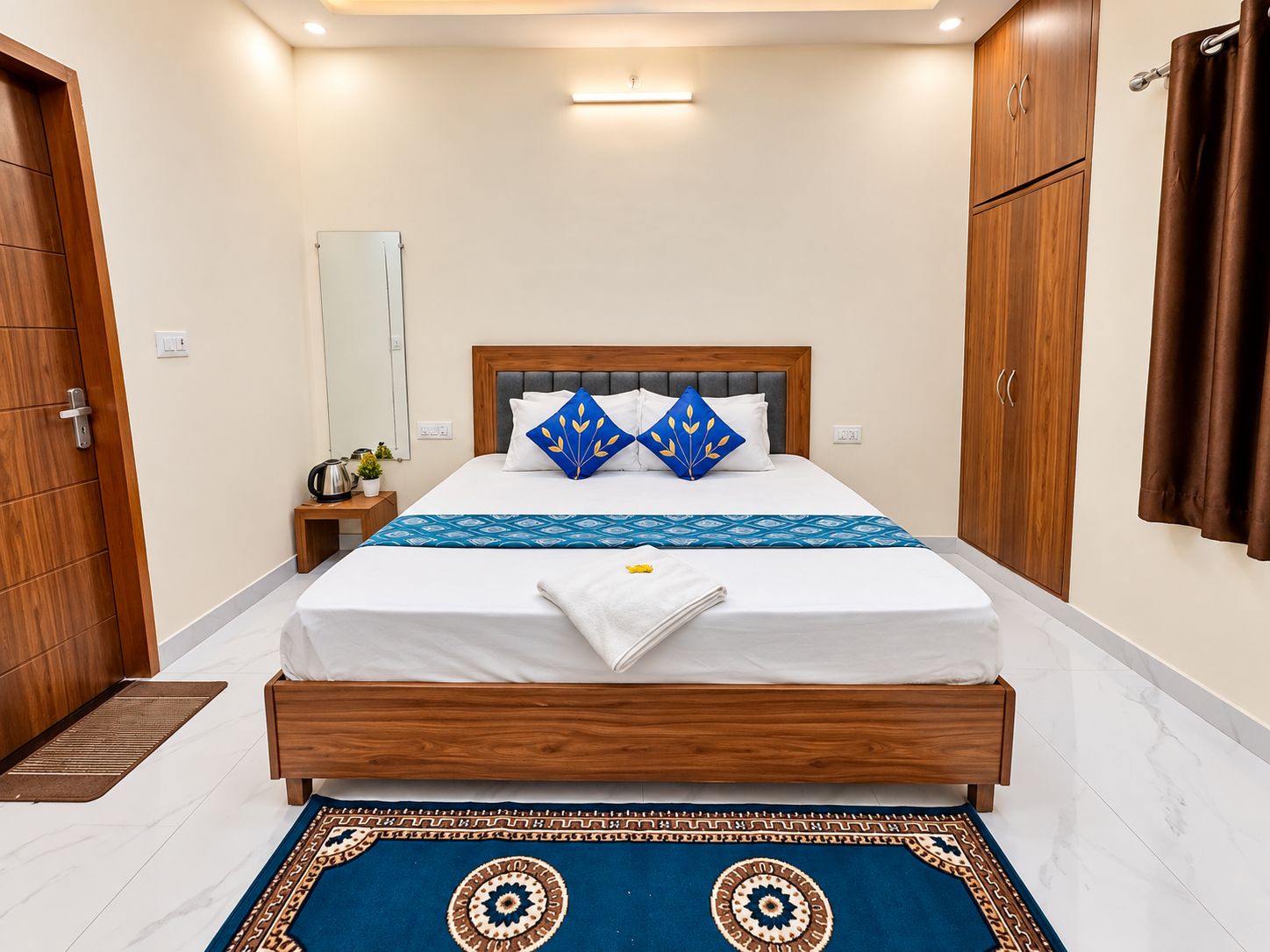 A hotel room with a wooden bed, a bedside table with a kettle, and a large mirror on the wall.
