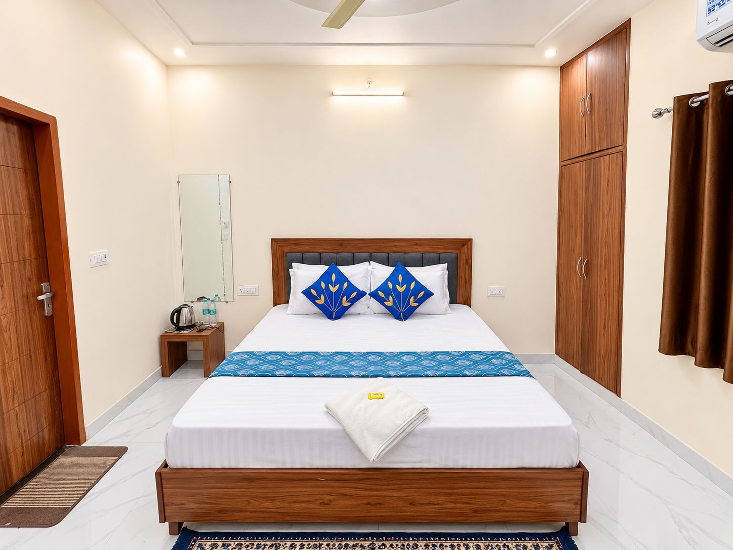 A hotel room with a bed, wooden wardrobe, a mirror, and a bedside table with a kettle and water bottles.