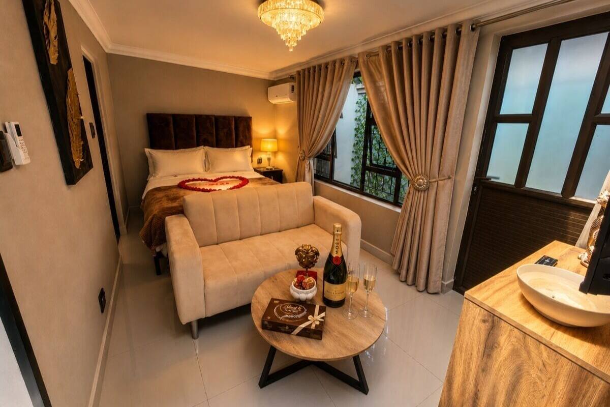 Hotelkamer met een bed, een slaapbank, een ronde salontafel met een fles en glazen, een houten bijzettafeltje en uitzicht op groen door het raam.