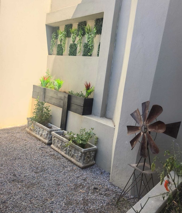 A courtyard with a windmill, planters with various plants, and a wall with a window. - Bryanston Palms Accommodation (Sandton)