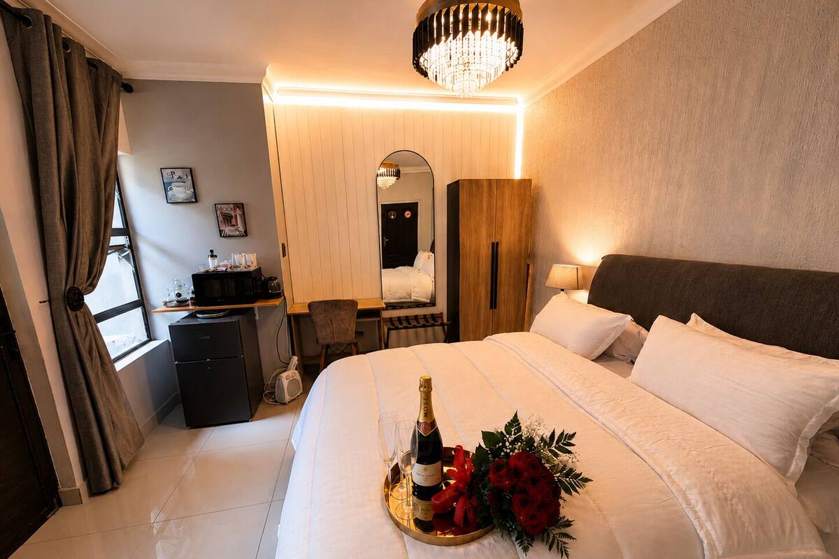 Een hotelkamer met een bed, een bureau met een computer, een spiegel, een kroonluchter en een raam met gordijnen.