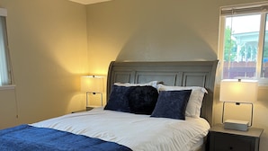 Un lit bien fait, recouvert d’une couverture bleue, avec deux lampes de chevet et une table de chevet sur laquelle se trouve une boîte.
