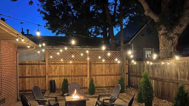 Un jardin avec un foyer, quatre fauteuils Adirondack et des guirlandes lumineuses.