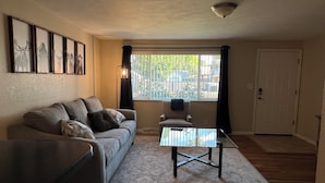 Un salon comprenant un canapé, une table basse, un fauteuil, une fenêtre avec des rideaux et des tableaux encadrés accrochés au mur.