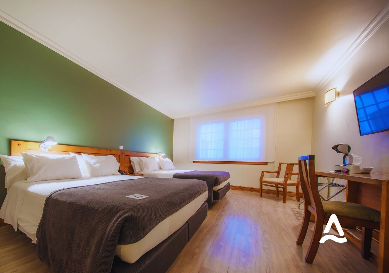 A hotel room with two beds, a desk with a chair, a TV, and a window with blinds.