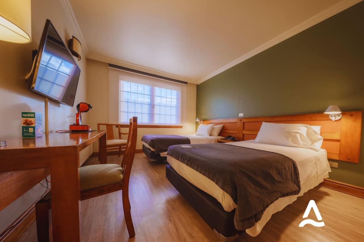 A hotel room with two beds, a desk with a computer, a chair, and a TV mounted on the wall.