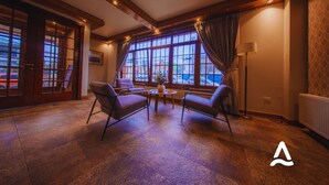 Une pièce spacieuse avec de grandes fenêtres, un plancher en bois et un coin salon comprenant deux fauteuils et une table.