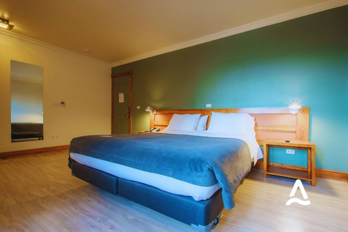 A bedroom with a large bed, a nightstand, a wall-mounted TV, and a wooden headboard.