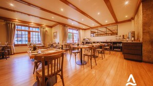 Un vaste espace dédié à la salle à manger, avec des tables et des chaises en bois, de grandes fenêtres dotées de rideaux et un mur en pierre sur l’un des côtés.