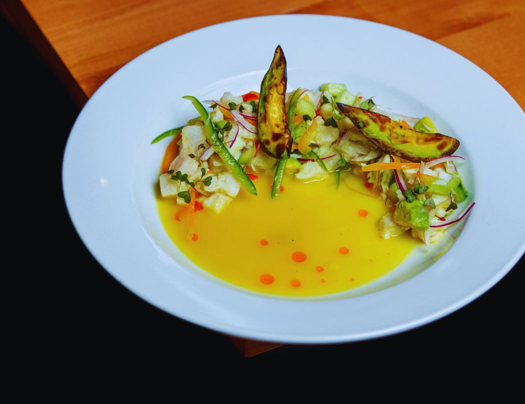 A white plate with a salad and a yellow sauce on a wooden table.