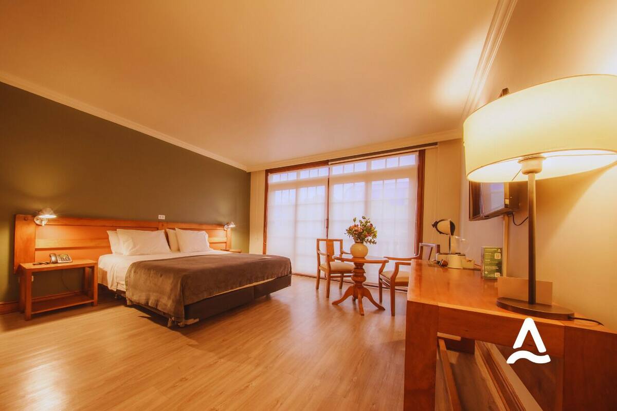 A hotel room with a bed, bedside table, lamp, desk, chair, and a TV.